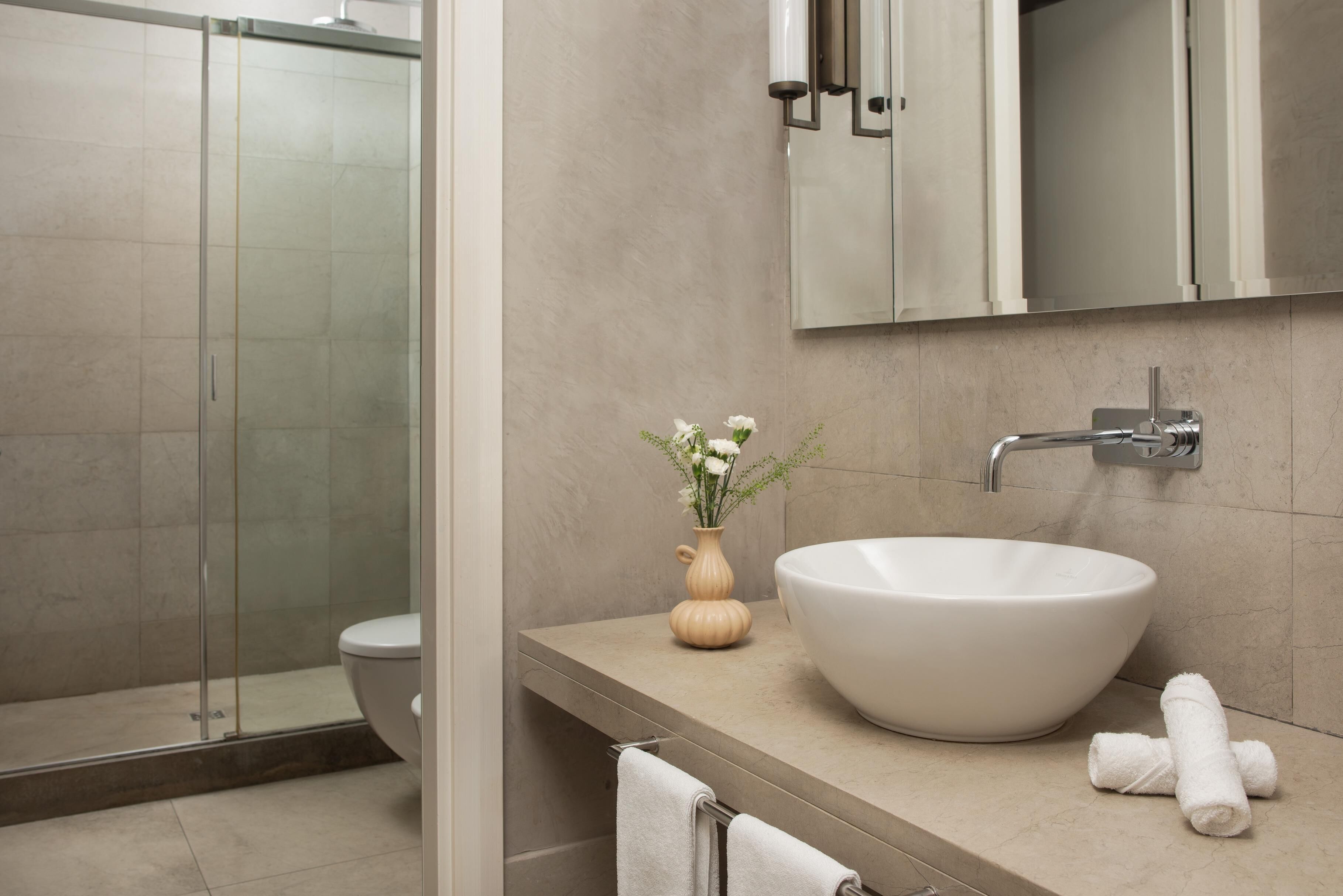 Un baño moderno con un lavabo de diseño, una cabina de ducha con paredes de vidrio y un pequeño florero con flores en la encimera.