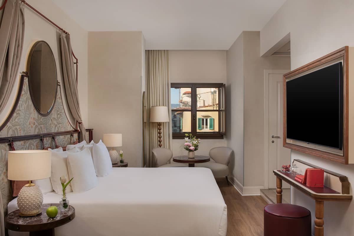 A hotel room with a bed, bedside table, lamp, chair, round table, and a TV.