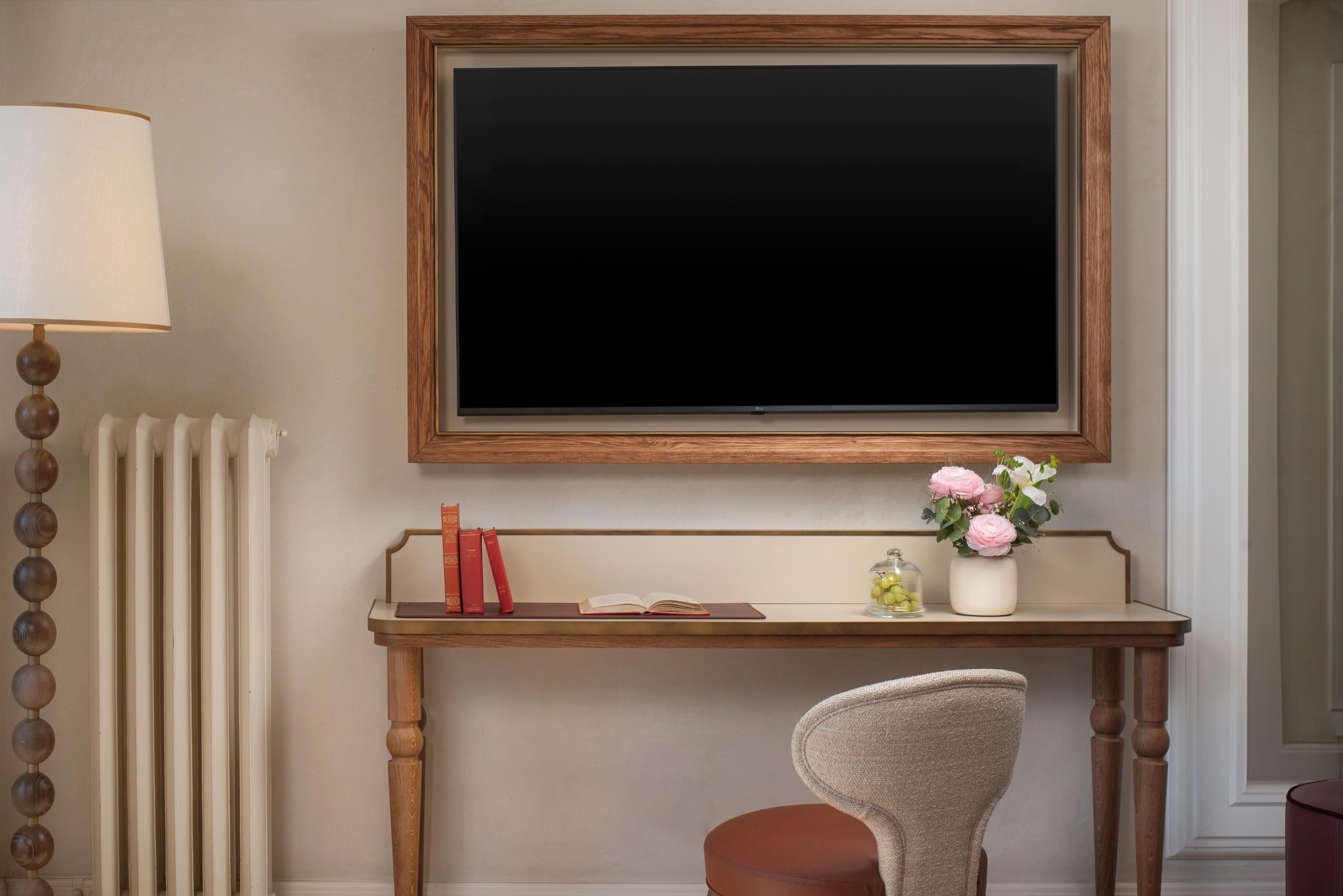 A room with a wooden desk, a chair, a radiator, a lamp, and a TV mounted on the wall.