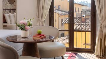 Ein Hotelzimmer mit Balkon, einem runden Tisch mit Blumenvase, einem Buch und einem Apfel.