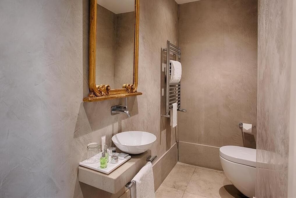 A modern bathroom with a large mirror, two sinks, a toilet, and a towel rack.