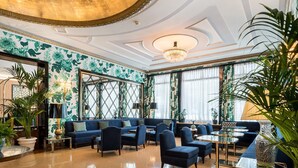Un hall d’entrée spacieux, avec un canapé bleu, des fauteuils et un lustre.