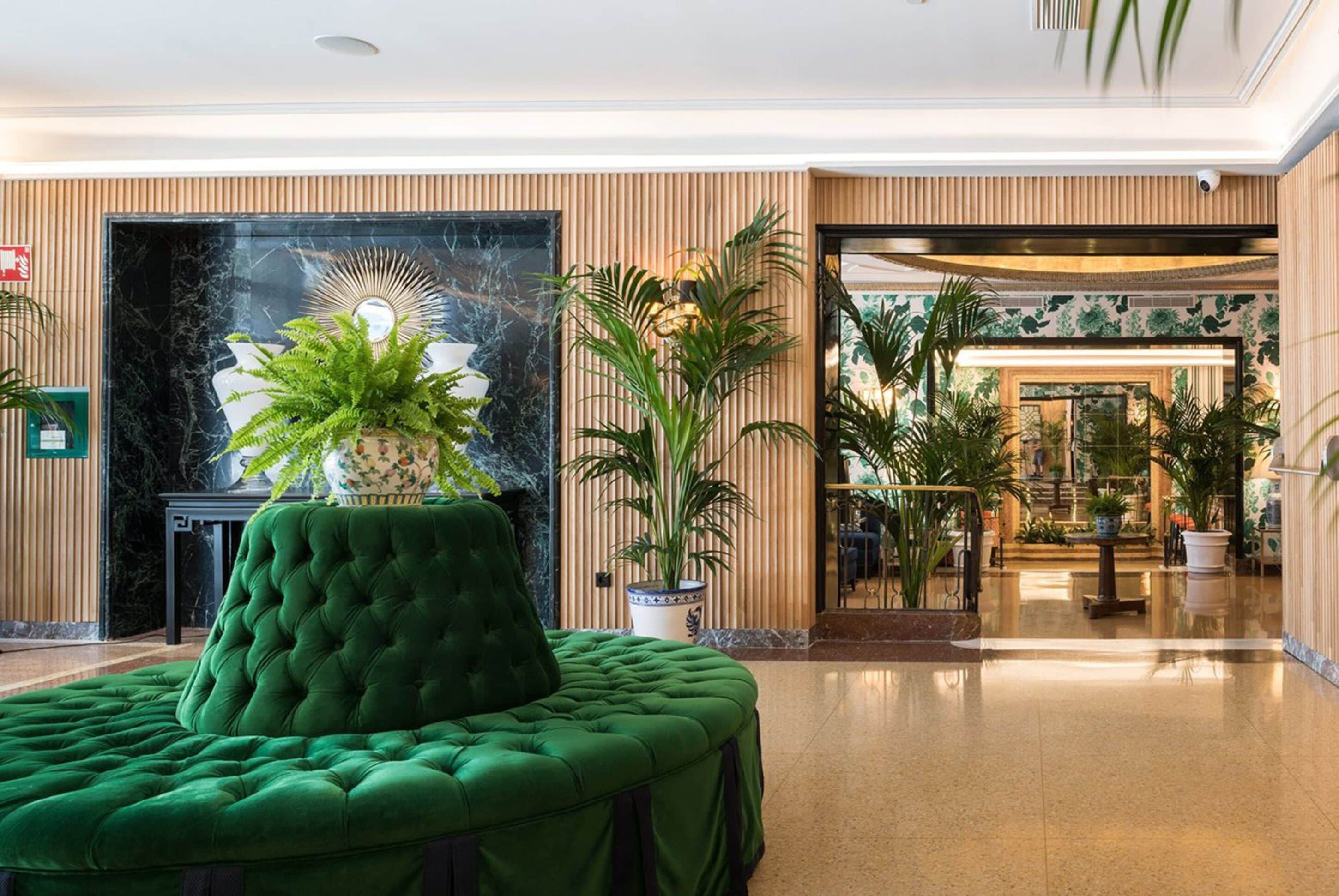 Un vestíbulo con un sofá verde capitonado, una planta grande en maceta, una chimenea de mármol y vistas hacia un comedor.