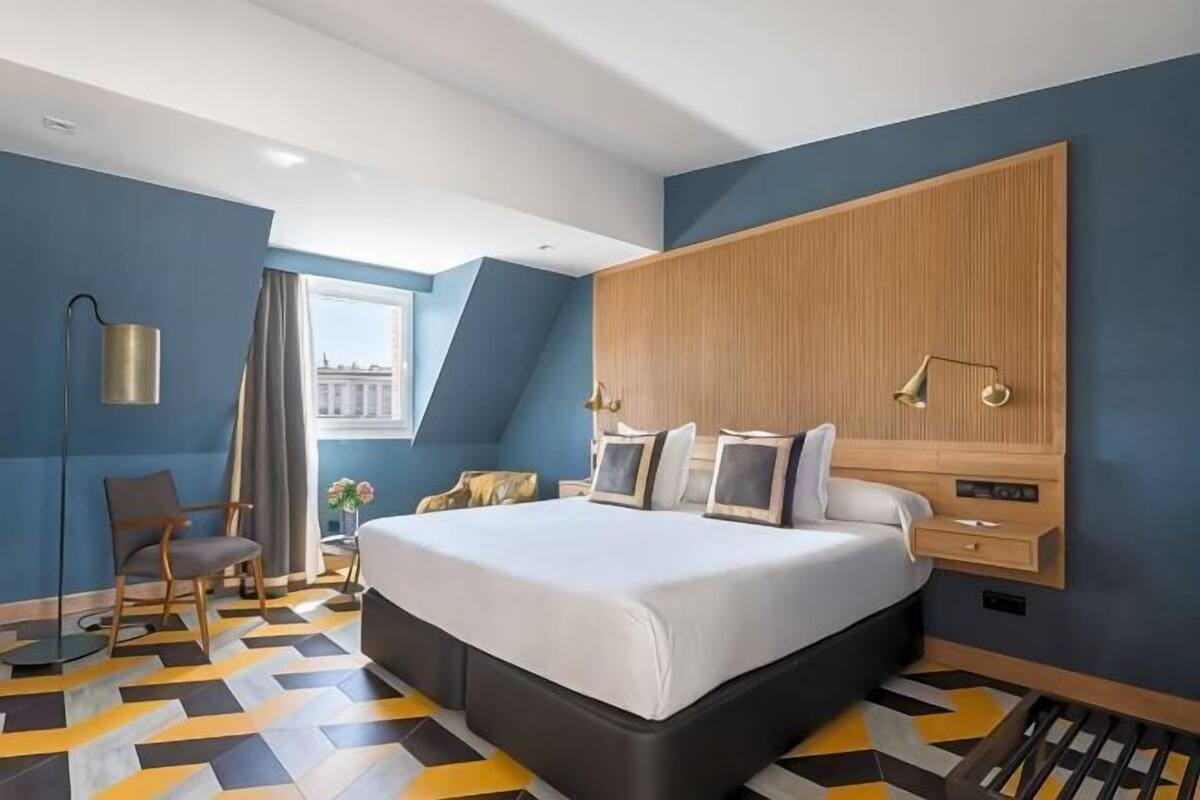 A modern hotel room with a large bed, a wooden headboard, a desk, and a view of the city.