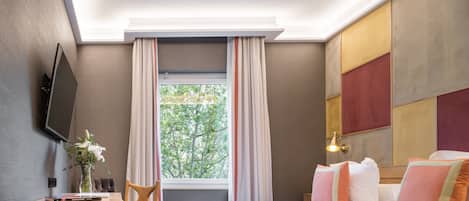 Habitación de hotel con cama, escritorio, silla, televisor montado en la pared y ventana con cortinas.