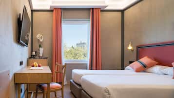 Ein Hotelzimmer mit einem Bett, einem Schreibtisch mit einem Laptop, einem Sessel, einem Fenster mit Vorhängen und Blick auf ein Gebäude.