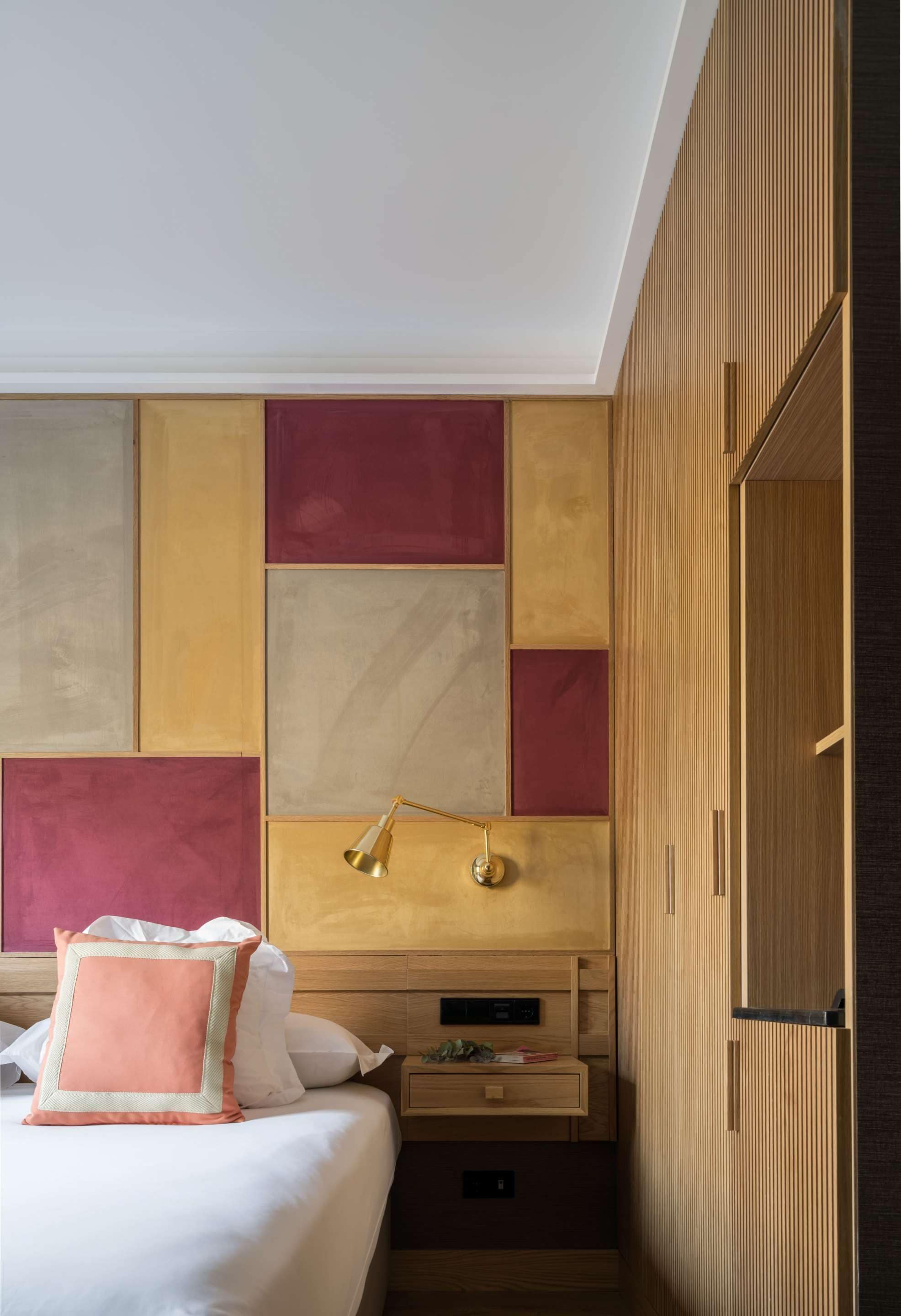 Une chambre d’hôtel moderne avec un grand lit, une armoire en bois et une table de chevet avec une lampe.