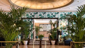 Un hall d’entrée avec un grand escalier, de grandes plantes en pot et un canapé bleu.