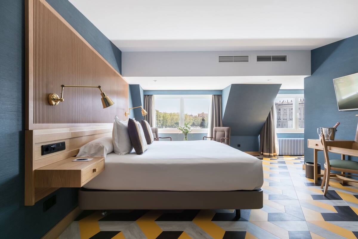 A modern hotel room with a large bed, a desk, and a view of the city.