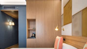 Una habitación de hotel moderna con una cama grande, un armario empotrado, una pequeña kitchenette y un espejo amplio.