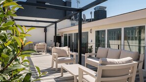 Une terrasse extérieure avec des meubles blancs, un mur de verre et un bâtiment moderne en arrière-plan.