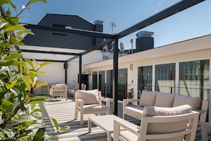 An outdoor patio with white furniture, a glass wall, and a modern building in the background.