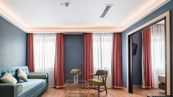 A modern living room with a blue sofa, a green chair, a glass coffee table, and red curtains.