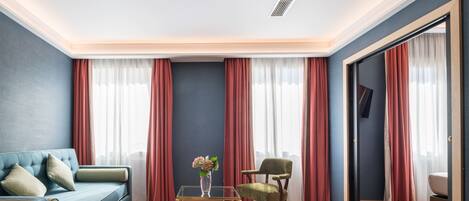A modern living room with a blue sofa, a green chair, a glass coffee table, and red curtains.
