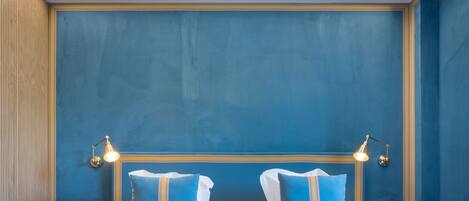 A hotel room with a blue accent wall, a wooden panel wall, a bed with white and blue bedding, and two bedside lamps.