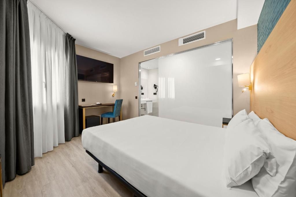 Ein Hotelzimmer mit Bett, Schreibtisch, Stuhl und einem großen Spiegel.