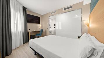 A hotel room with a bed, a desk, a chair, and a large mirror.