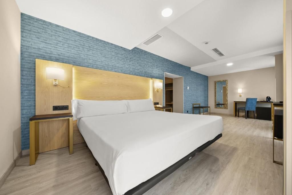 Una habitación de hotel con una cama grande, mesitas de noche, un escritorio y una silla.