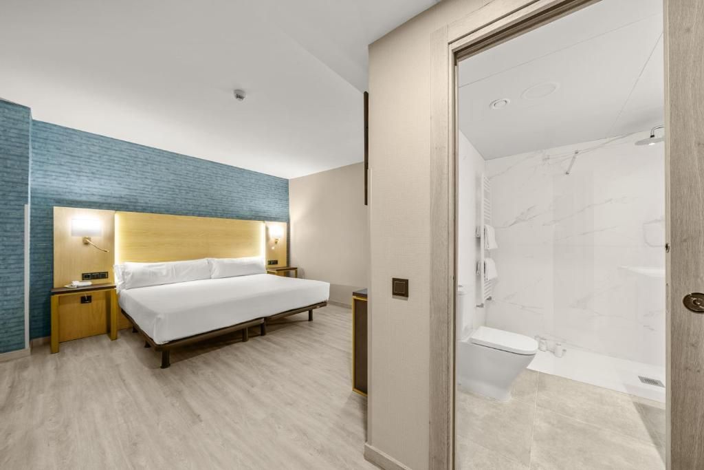 Hotellihuone, jossa on sänky, yöpöydät, suihku ja kylpyhuone.