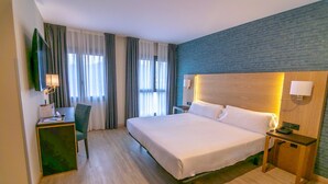 A hotel room with a large bed, a desk with a chair, a TV mounted on the wall, and a nightstand with a lamp. - Hotel Zentral Ramiro I Oviedo (Oviedo)