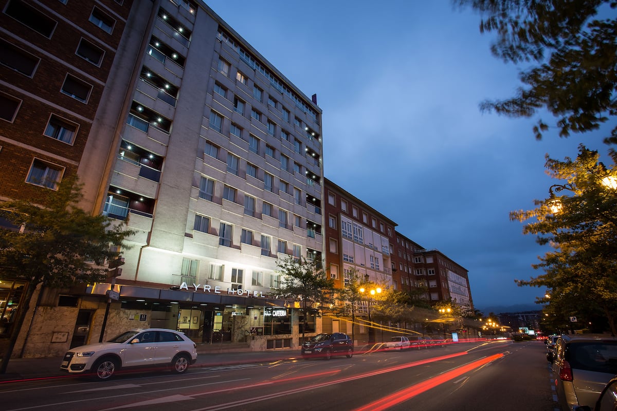 Un hôtel à plusieurs étages, doté d’une façade moderne, d’un restaurant bien visible et d’une rue bien éclairée au crépuscule.