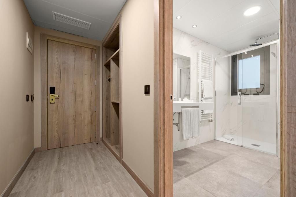 Een gang die leidt naar een badkamer met een douche, toilet en wastafel.