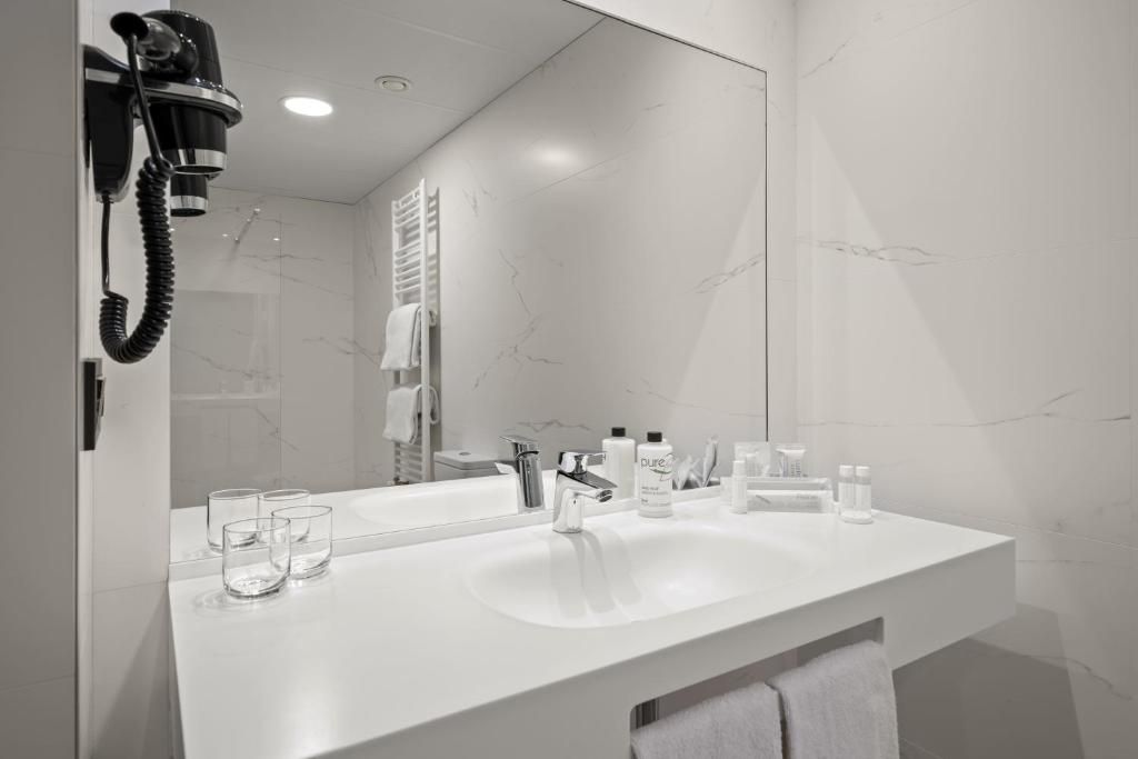 A modern bathroom with a white sink, a large mirror, and a hairdryer mounted on the wall.
