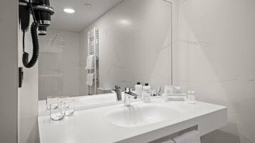 A modern bathroom with a white sink, a large mirror, and a hairdryer mounted on the wall.