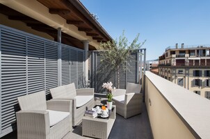 Een balkon met rieten meubilair, een bloemenvaas en een tafel met boeken en een theepot.