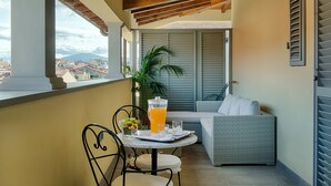 Un balcón con un sofá de mimbre, una mesa con una jarra de jugo de naranja y vistas a un paisaje urbano.