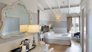 Habitación de hotel con un espejo grande y ornamentado, cama con ropa de cama blanca, mesita de noche con lámpara, bandeja con artículos de desayuno y vista al balcón.