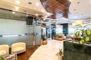 Un vestíbulo moderno con puertas de vidrio, una mesa de recepción y zonas de estar.
