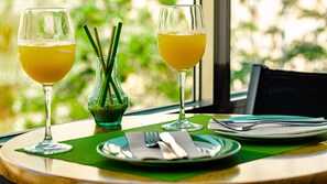 Two glasses of orange juice on a table with a green placemat, a green vase with green leaves, and a plate with cutlery. - Hotel Regio Cadiz (Cádiz)