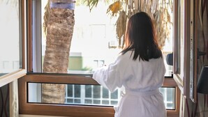 A person in a white robe standing by an open window with a view of palm trees and a building outside. - Hotel Regio Cadiz (Cádiz)
