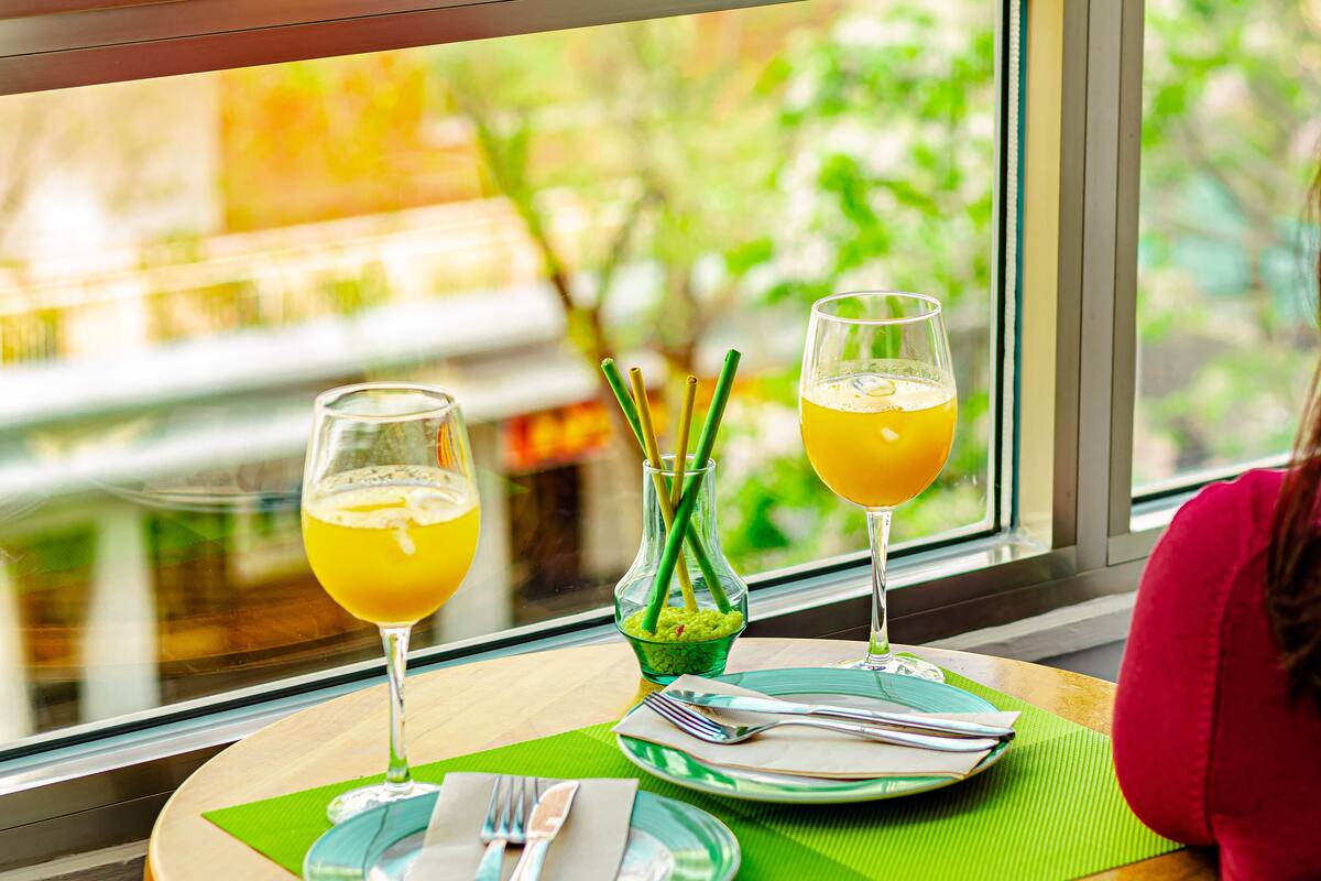 A dining table with two glasses of orange juice, a green bowl, and a green placemat.