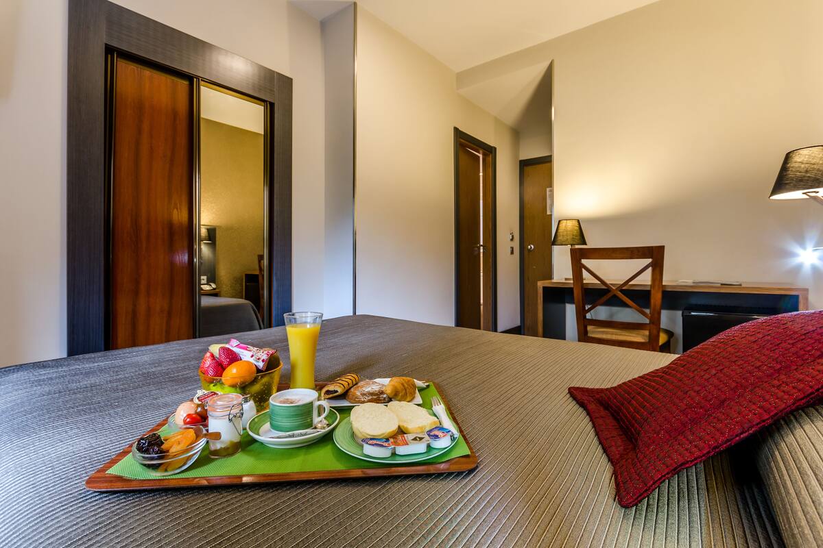 A hotel room with a neatly made breakfast tray on the bed, a lamp, and a chair.