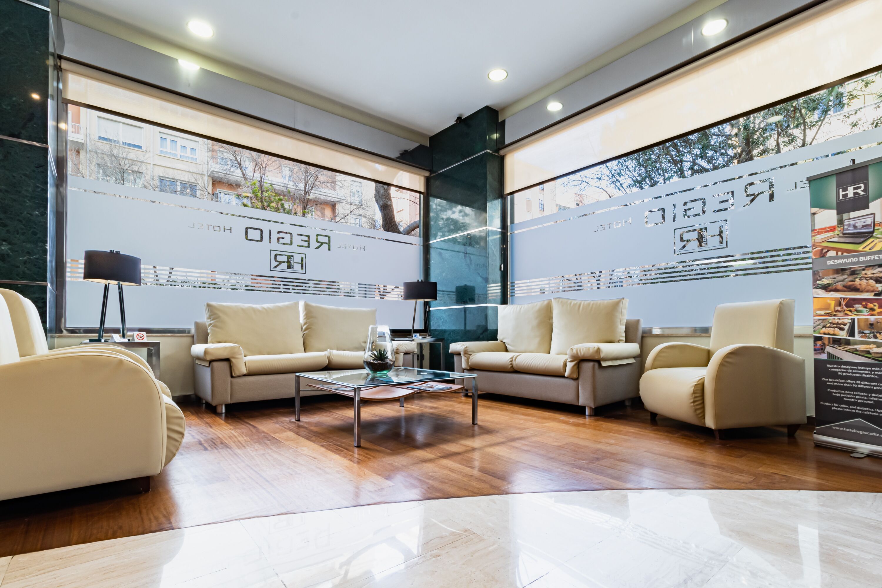 A modern hotel lobby with two sofas, a coffee table, and large windows with city views.