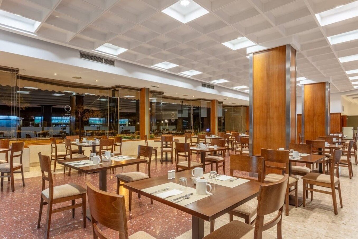 A spacious dining area with multiple tables and chairs, large windows, and a high ceiling with skylights.