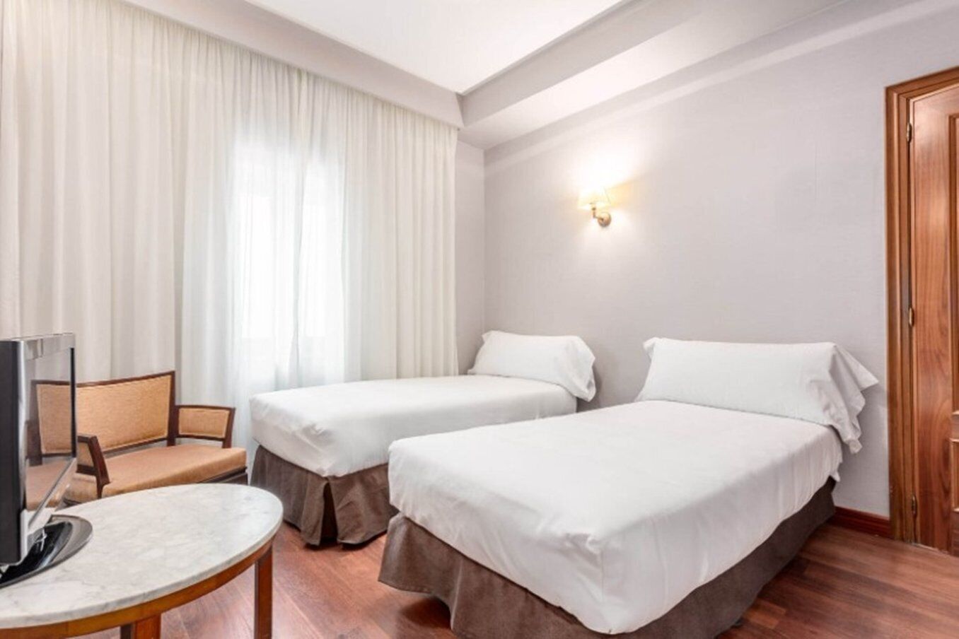 Habitación de hotel con dos camas individuales, una mesita, una silla y un televisor.