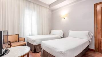 Habitación de hotel con dos camas individuales, una mesita, una silla y un televisor.