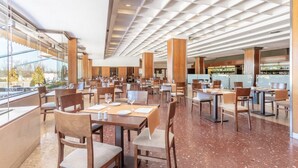 Un restaurante amplio con varias mesas y sillas, un techo alto con diseño de cuadrícula y ventanas grandes que ofrecen vistas al exterior.