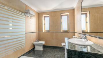 A modern bathroom with a glass shower enclosure, a bidet, a sink with a mirror, and a window with a view.