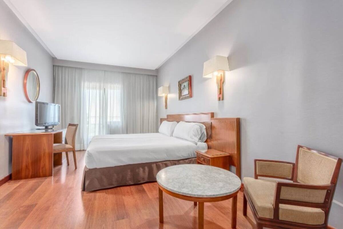 Habitació d'hotel amb un llit gran, un escriptori amb cadira, una taula rodona petita i una televisió.
