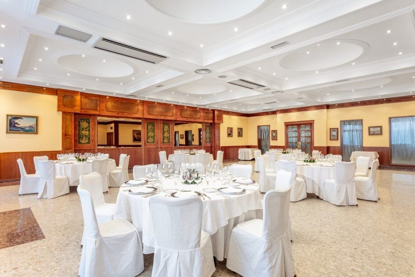 A spacious banquet hall with round tables set for dining, white chairs, and a polished floor.