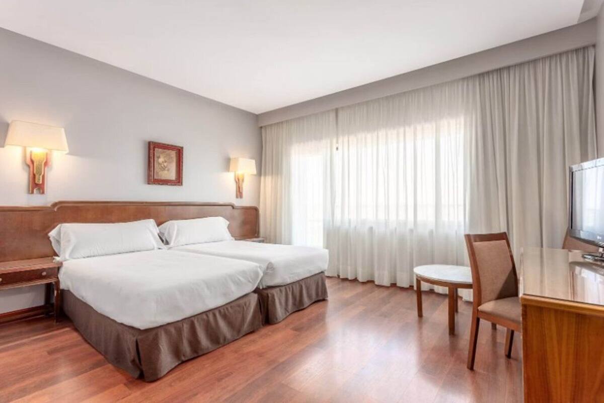 Habitació d'hotel amb dos llits, una taula, una cadira i un televisor.