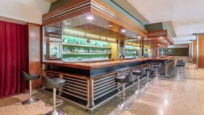 Una zona de bar con mostrador, taburetes y estanterías llenas de botellas.