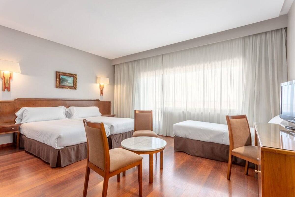 Una habitació d'hotel amb dos llits, una taula rodona i dues cadires.