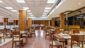 A spacious restaurant with wooden tables and chairs, a central buffet, and large windows offering a view of the cityscape.
