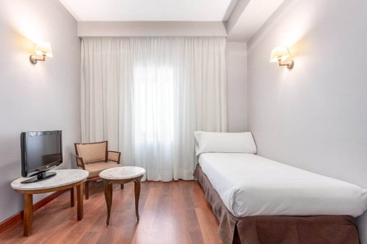 Habitació d'hotel amb un llit, una televisió, una cadira i una taula petita.