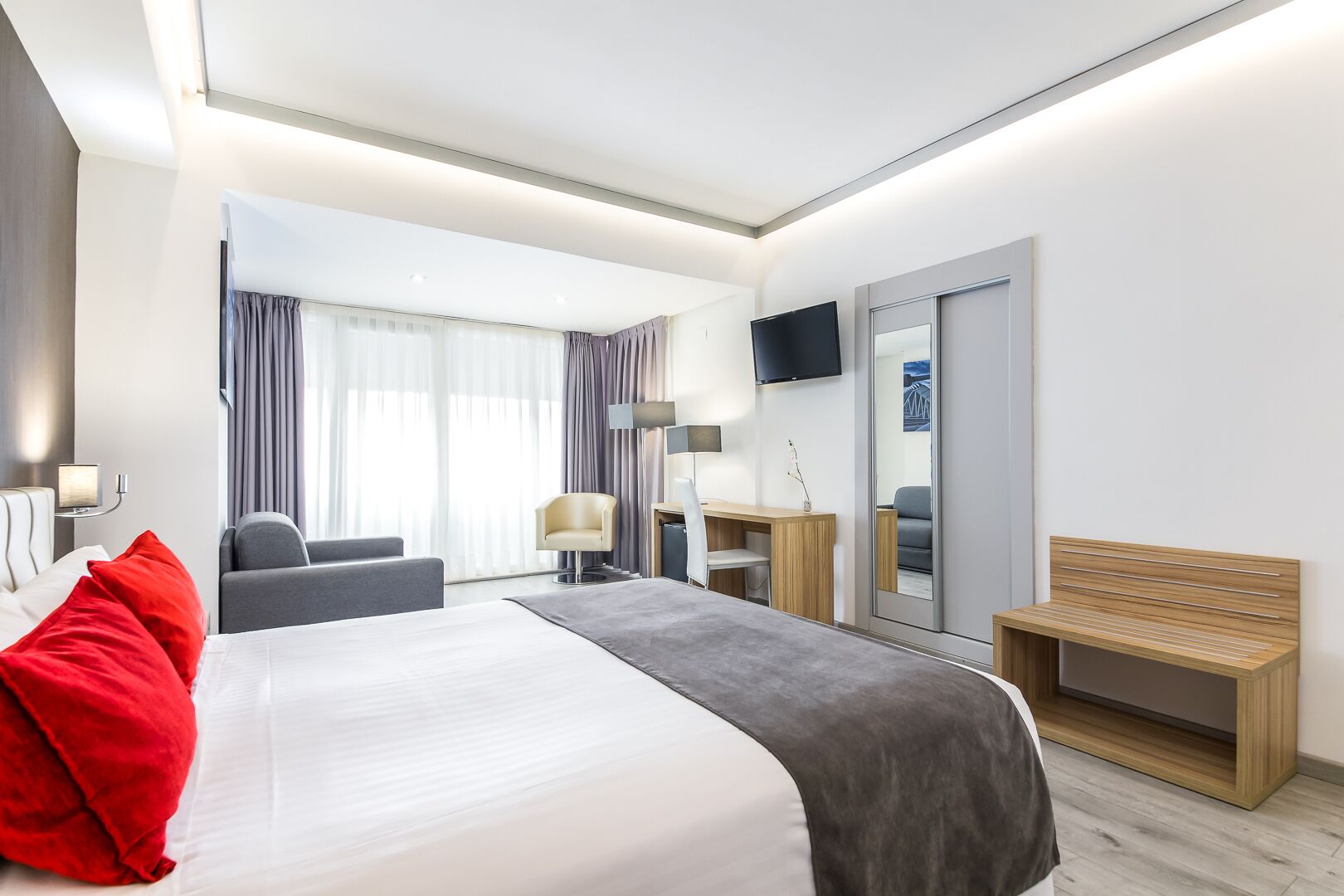 Una habitación de hotel moderna con una cama grande, un escritorio, una silla, un televisor y un espejo.